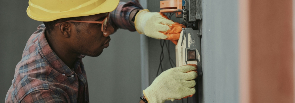 An electrician, wearing a hardhat and safety gloves, working on some electrical wiring