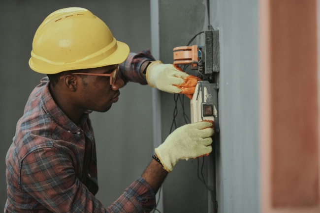 An electrician, wearing a hardhat and safety gloves, working on some electrical wiring