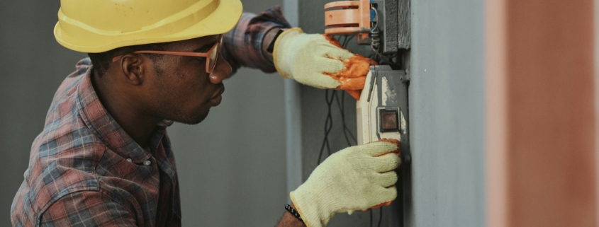 An electrician, wearing a hardhat and safety gloves, working on some electrical wiring