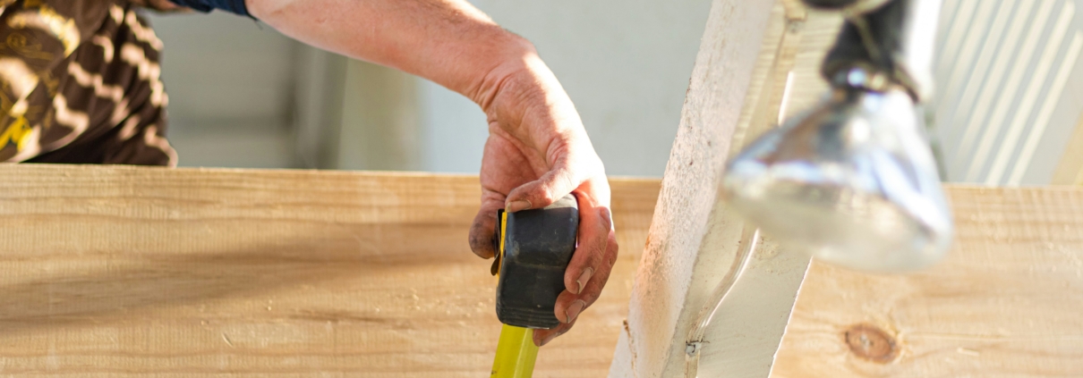 A person using a tape measure underneath some roof rafters with a cable tray and some lights wired in