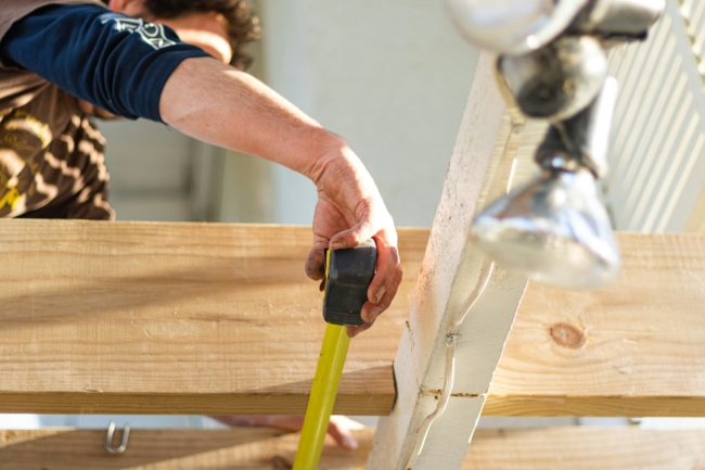 A person using a tape measure underneath some roof rafters with a cable tray and some lights wired in