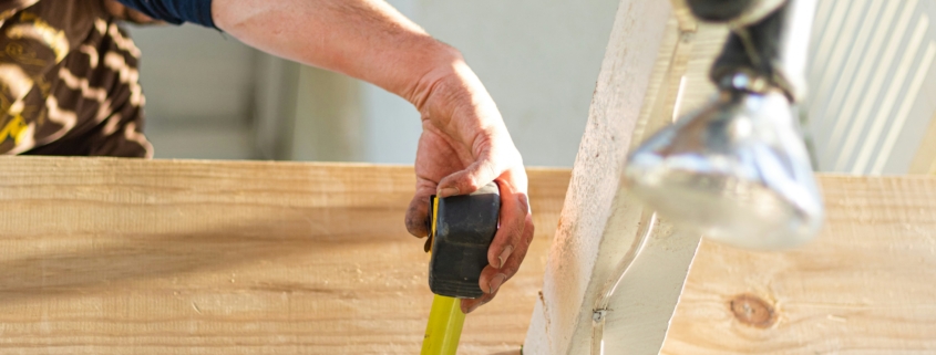 A person using a tape measure underneath some roof rafters with a cable tray and some lights wired in