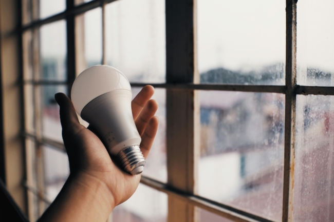 A person holding an energy efficient light bulb in front of a window