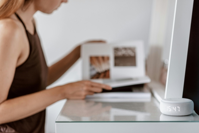 A lady sat at a vanity table with an Amazon Alexa on the table showing the time