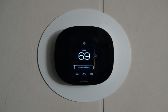 A black smart thermostat against a white wall