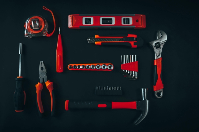 a set of red tools on a black worktop, including a set of pliers, a wrench, a hammer etc.