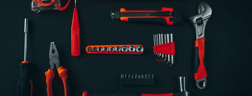 a set of red tools on a black worktop, including a set of pliers, a wrench, a hammer etc.