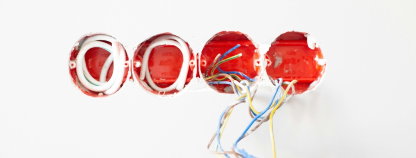 Four holes in a white wall with various wires hanging out during installation